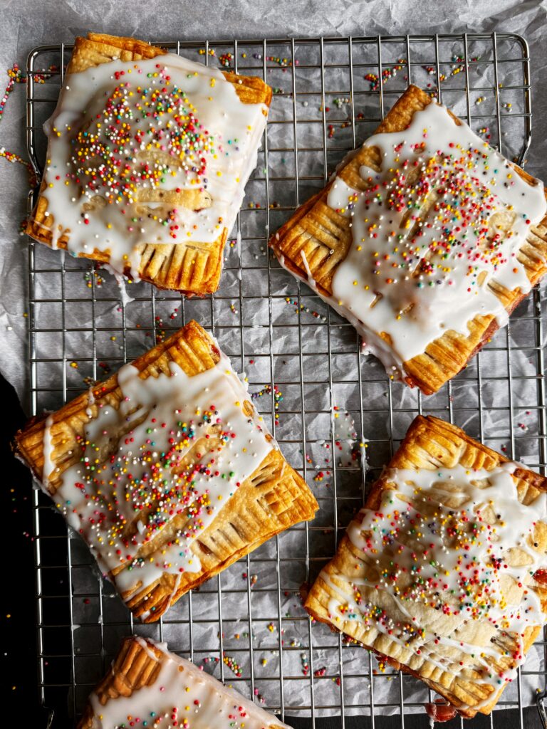 photo of homemade strawberry almond pop tarts sitting on a wire rack and parchment paper