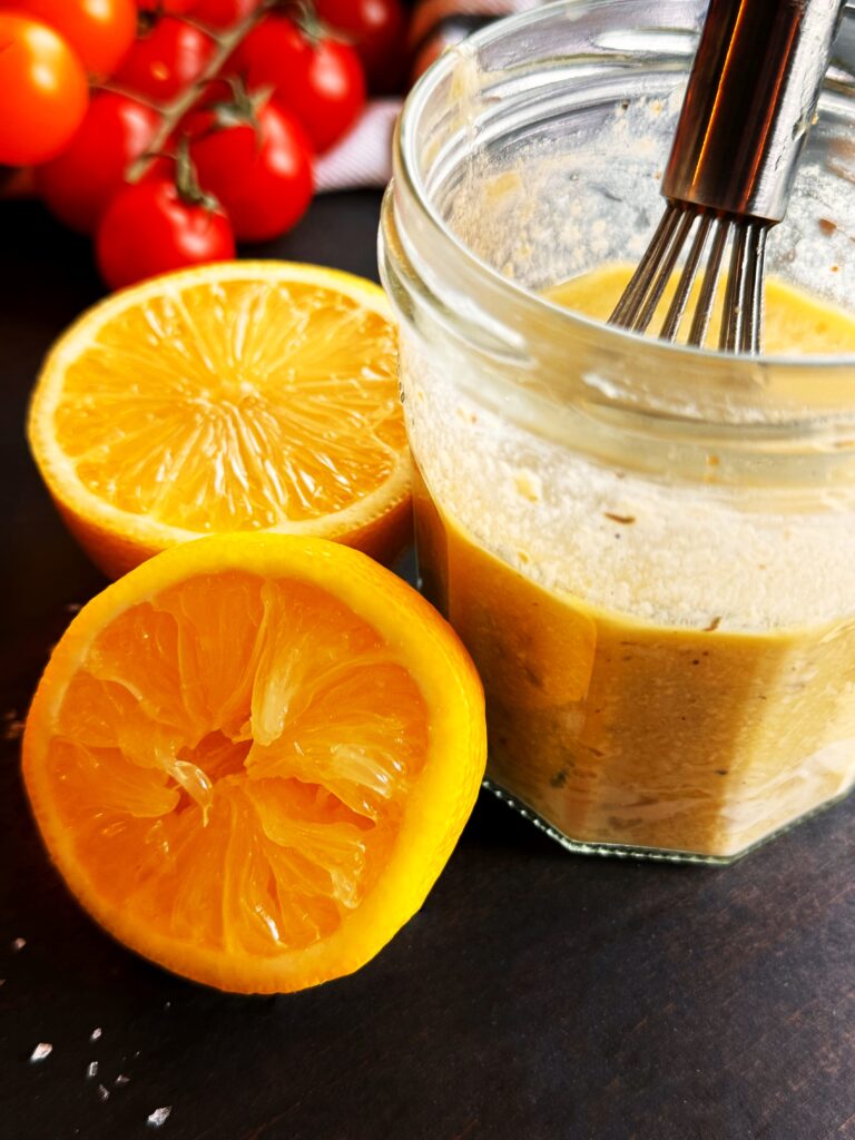 photo of a glass jar of lemon tahini salad dressing and two lemon halves and red cherry tomatoes on the vine