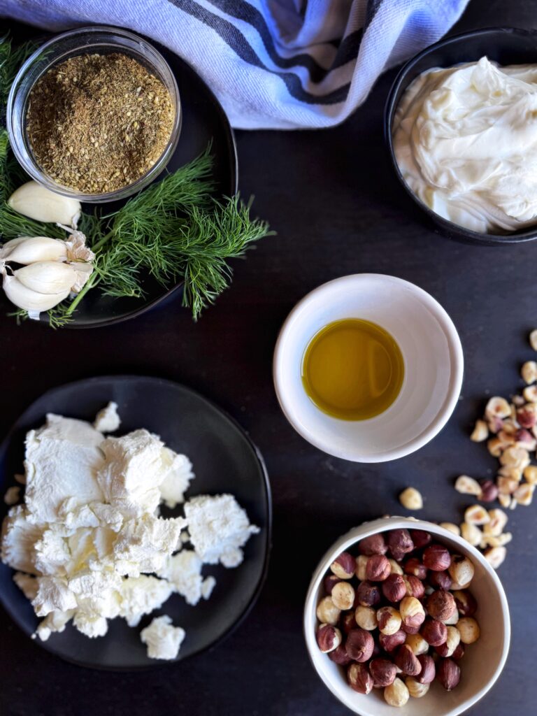 photo of small bowls filled with olive oil, crumbled goat cheese, chopped hazelnuts, Greek yoghurt, za'atar seasoning, garlic cloves, and fresh dill