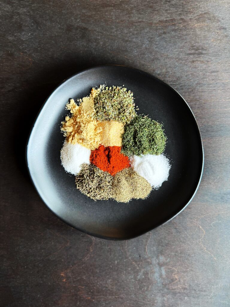 a photo of a black plate sitting on a dark brown wooden tabletop. The black plate is full of different herbs and spicdes.