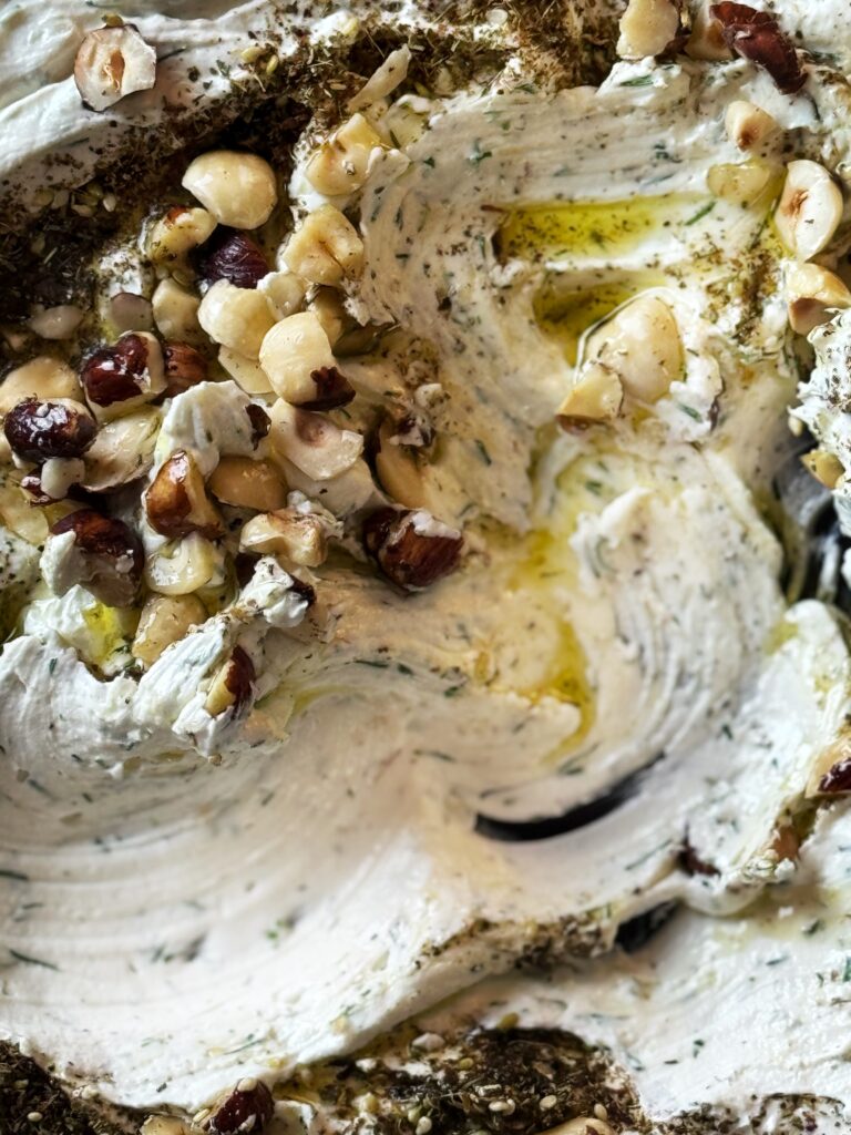 photo of whipped goat cheese spread topped with a drizzle of olive oil and a sprinkling of chopped hazelnuts and za'atar seasoning