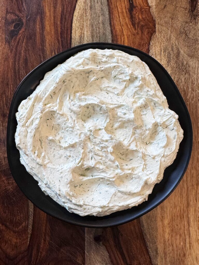 whipped goat cheese spread onto a black ceramic plate that is sitting on a wooden board.