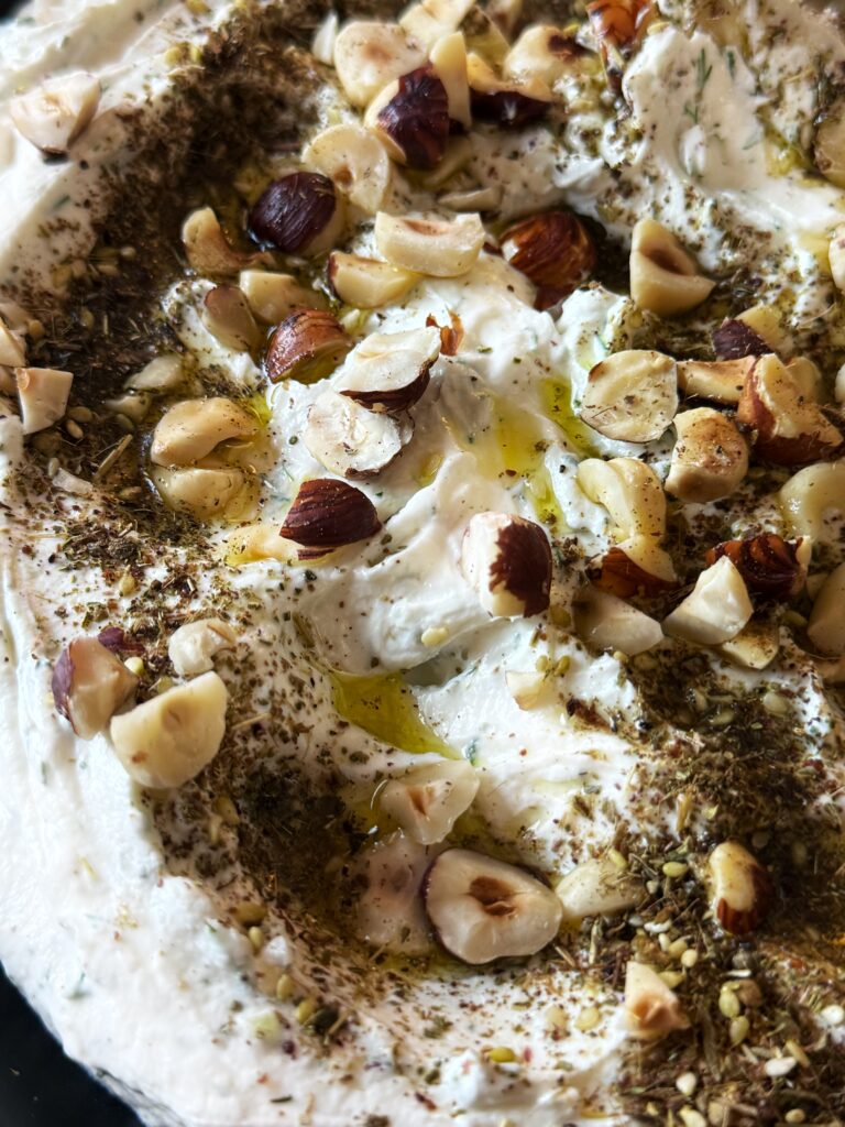 photo of whipped goat cheese spread topped with a drizzle of olive oil and a sprinkling of chopped hazelnuts and za'atar seasoning