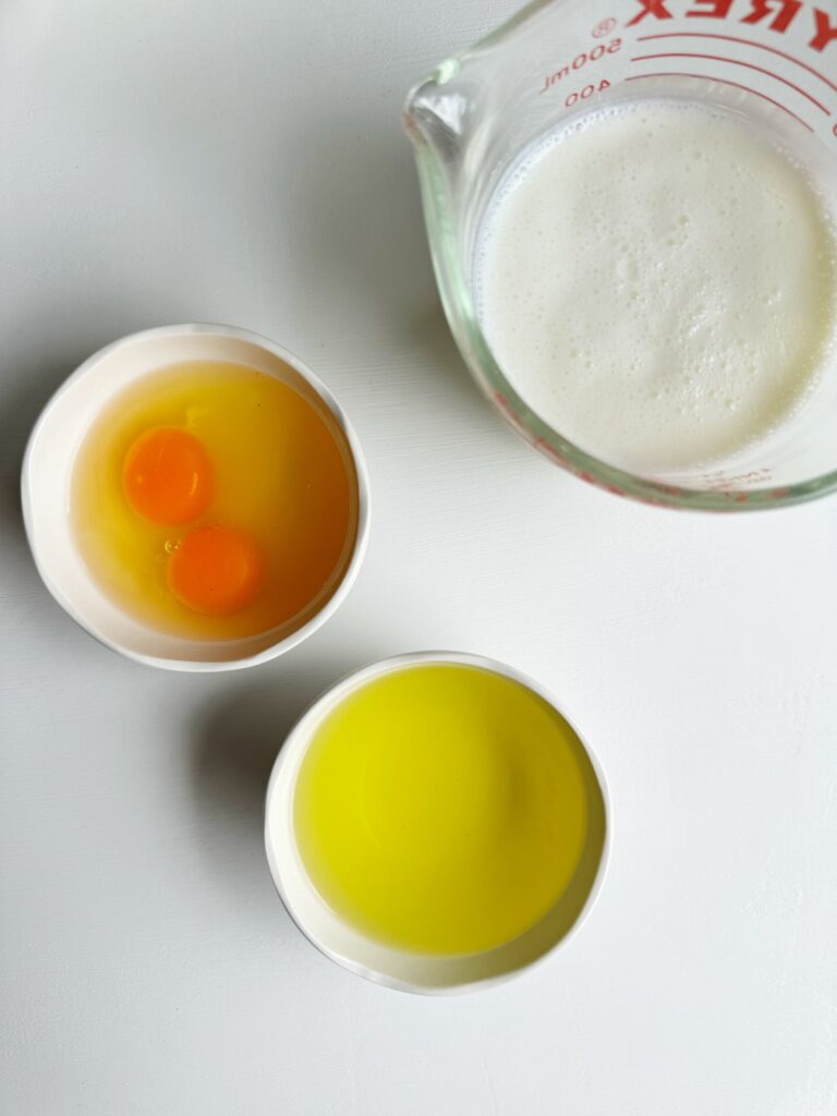 photo of white and clear bowls filled with pepperoncini brine, raw eggs, and buttermilk