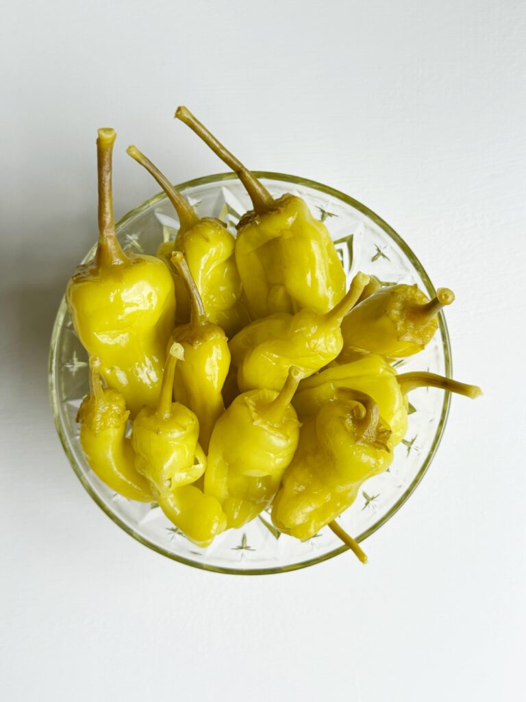 photo of a clear crystal bowl sitting on a white tabletop and filled with pepperoncini peppers