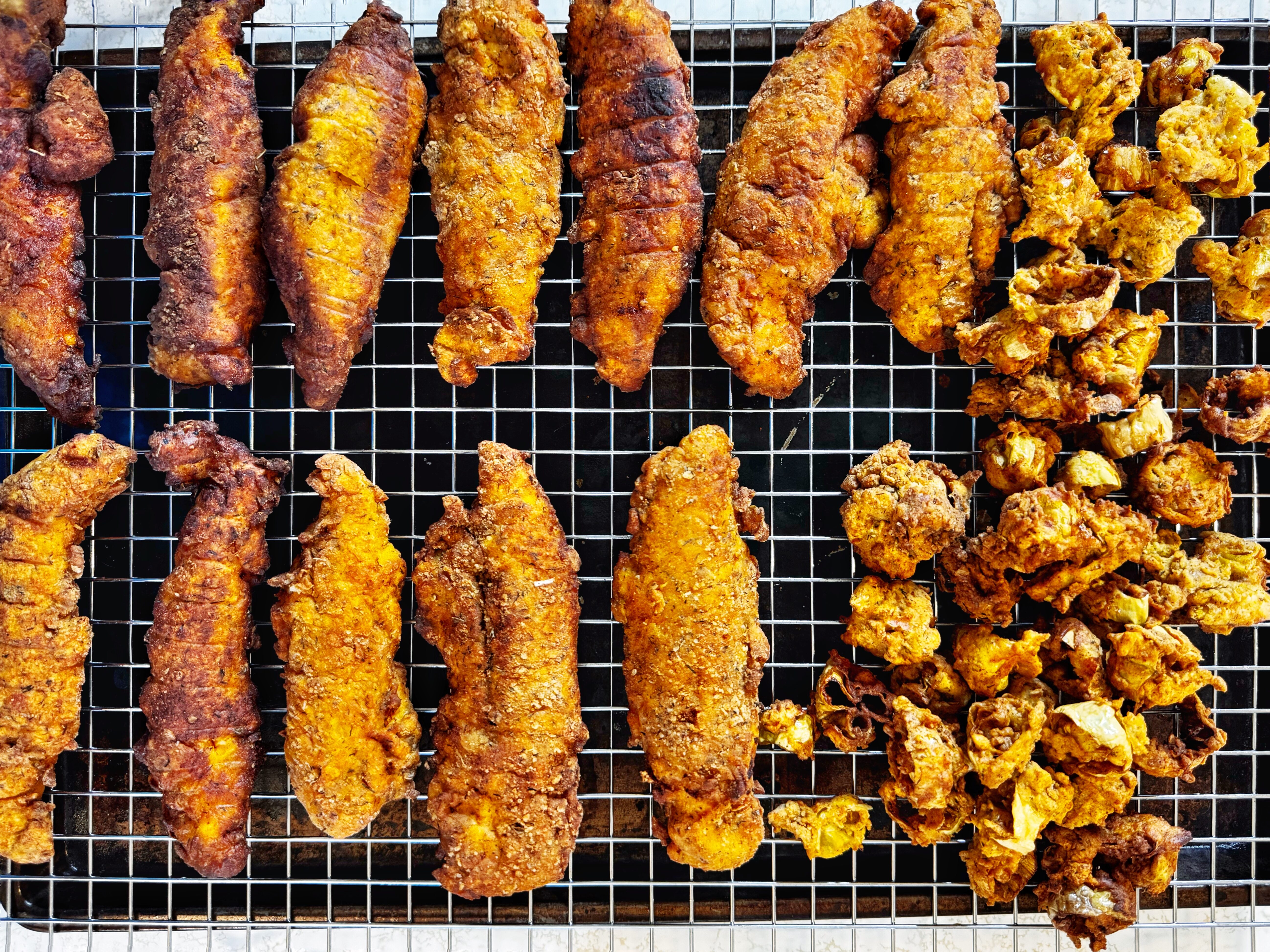 photo of fried chicken tenders and fried pepperoncini peppers, all sitting on a wire rack